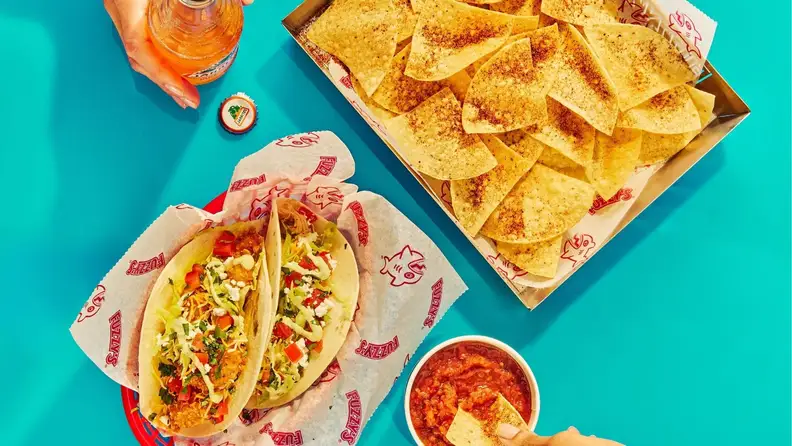 Two tacos and chips with salsa on a teal background