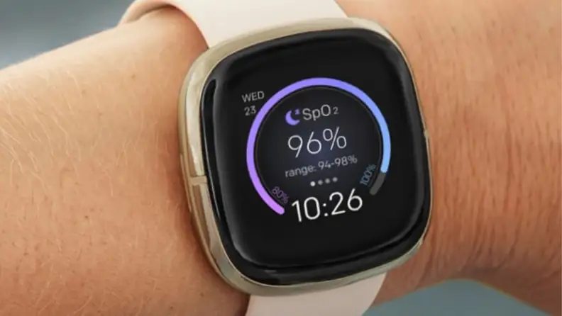 a woman's wrist showing the fitbit sense with a clock face illuminated