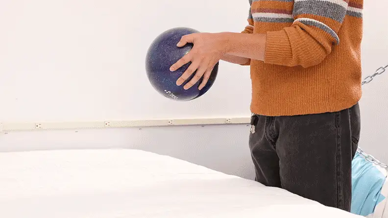 A moving image of a person dropping a bowling ball onto the surface of the Awara Premier mattress.