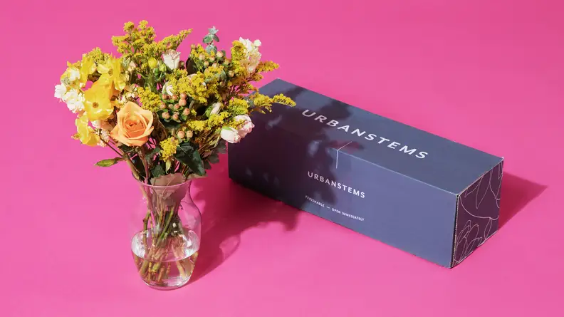 A vase of flowers next to the box they were shipped in.