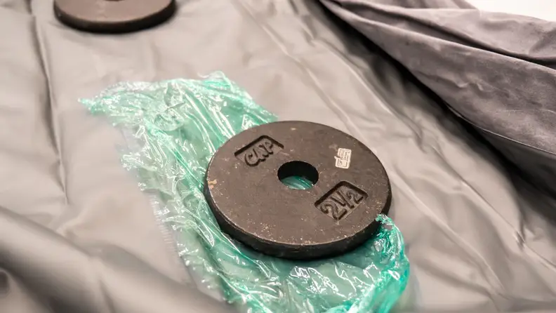 An iron weight next to the patched hole on the air mattress.