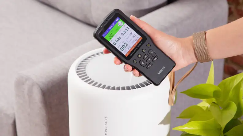 An air quality monitor is held up over the Molekule air purifier.