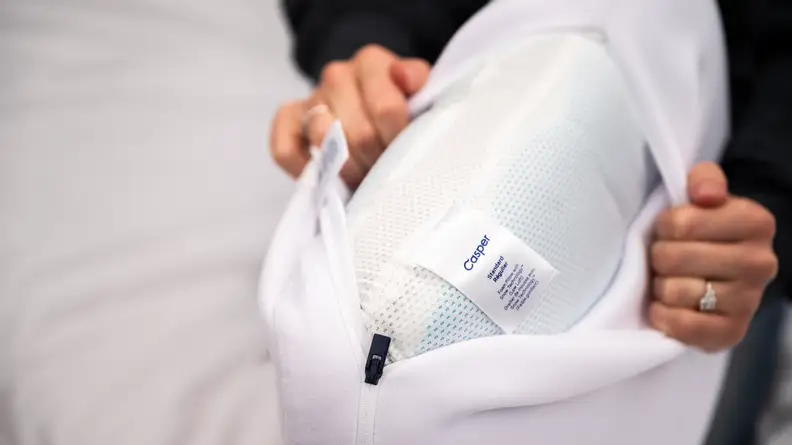 Person using hands to hold open pillow case with pillow inside.