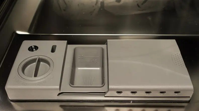 A rinse aid and detergent dispenser on the door of a dishwasher.
