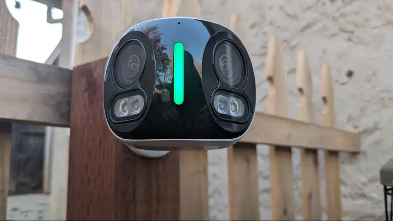The Lorex 4K Dual-Lens Wi-Fi Security Camera hanging on a fence post outdoors.