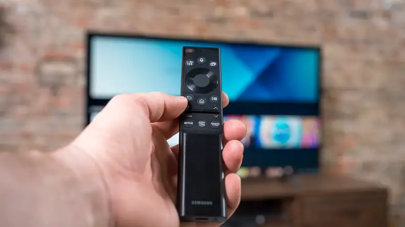 A man holds the Samsung TV remote in front of the screen