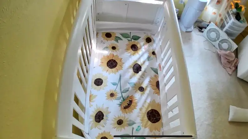 Daytime vision of empty crib using Owlet Dream Sight camera with yellow walls and sunflower sheets.
