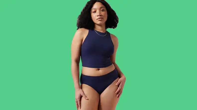 Black woman wearing navy tankini on green background.