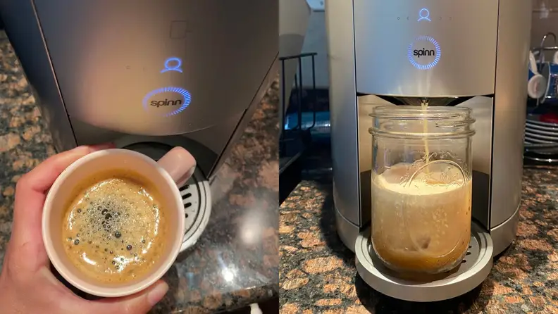 A person holds a cup of freshly brewed coffee from a coffee maker.