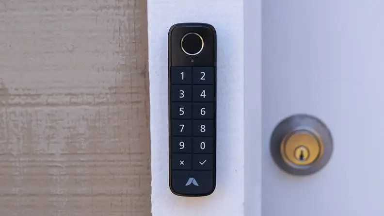 The Abode Lock Keypad mounted on a white wood door frame next to a key lock on a door.