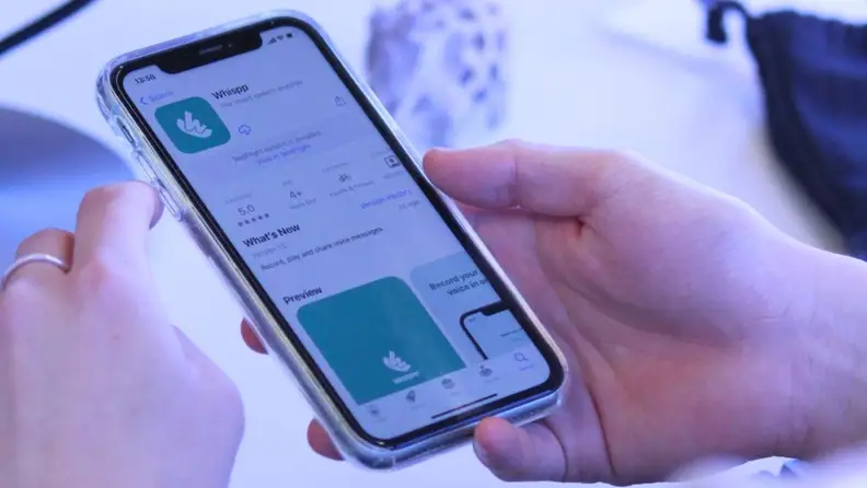 Close-up of a pair of hands holding a smartphone with the Whispp app called up on the Apple Store.