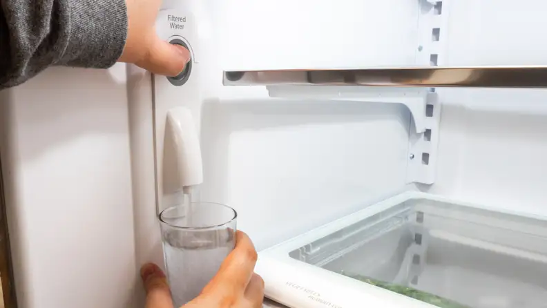 In close-up, someone pours a glass of water from a built-in refrigerator filter.