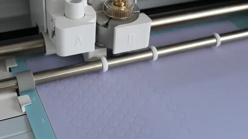 Close-up of embossed purple material in a Cricut machine.