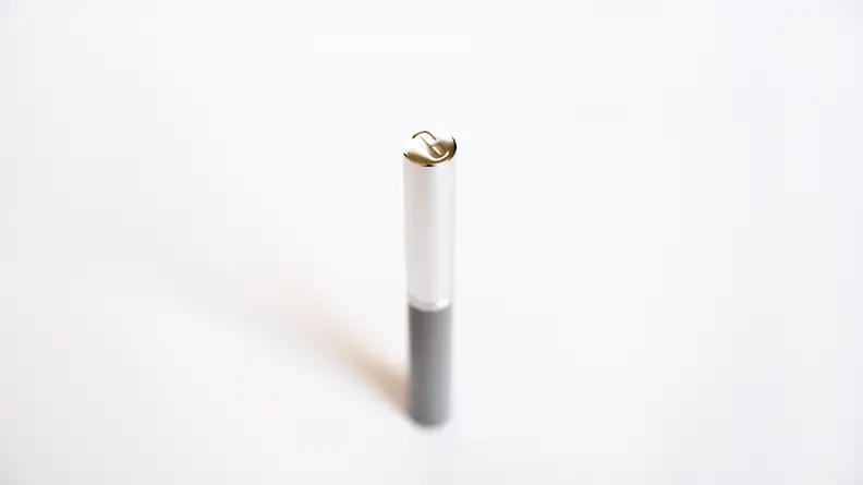 A silver tube of lipstick stands with its cap showing a "C" imprint.