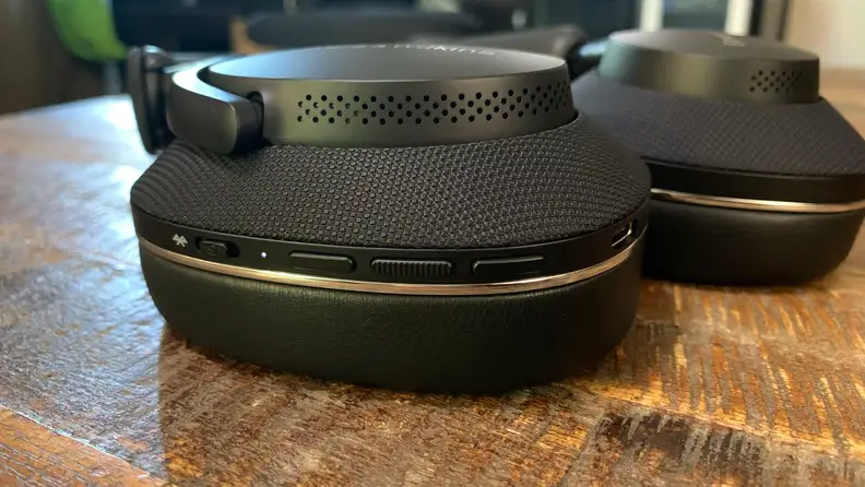 The Bowers & Wilkins Px7 S2 headphones lay on a wooden table with their button controls displayed.