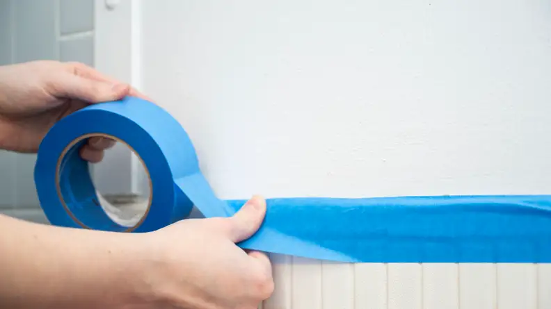 Person applying painter's tape onto wall to paint over