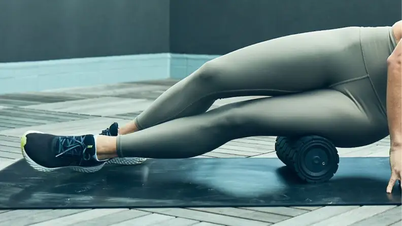 A woman rolling the side of her quad with the Therabody Wave Roller.