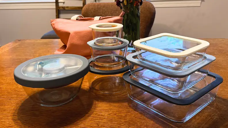 Six storage containers plus a salad storage container sit on a wooden table
