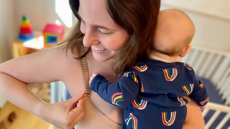 A parent clasps their Thirdlove 24/7 Classic Nursing Bra strap while holding an infant.