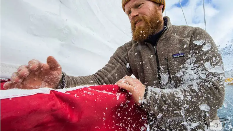 A mean wearing a sweater, clearing ice away outdoors.