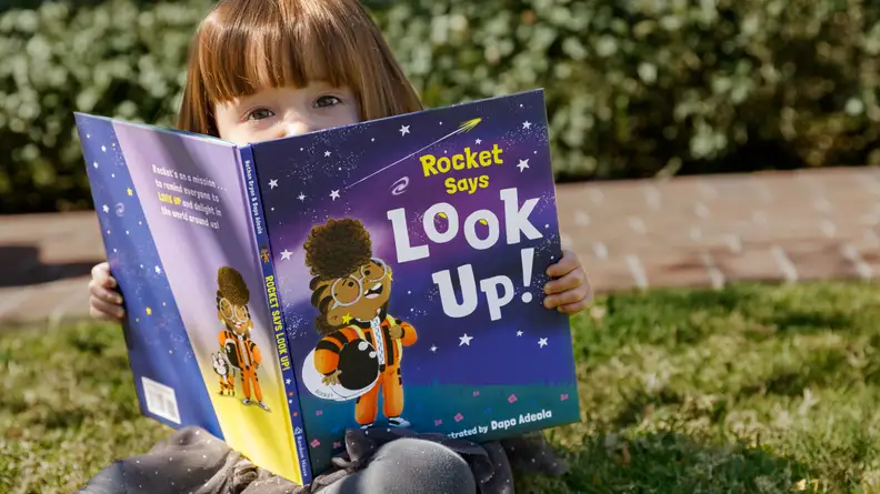 A child reads the book "Rocket Says Look Up!"