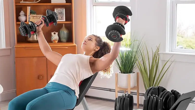 A woman doing chest flys with the Bowflex adjustable dumbbells.