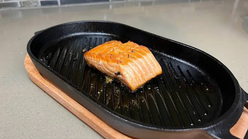 Small piece of cooked salmon on top of black grill pan.
