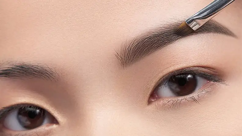 A woman fills in her brows with the Anastasia Beverly Hills Brow Powder Duo.