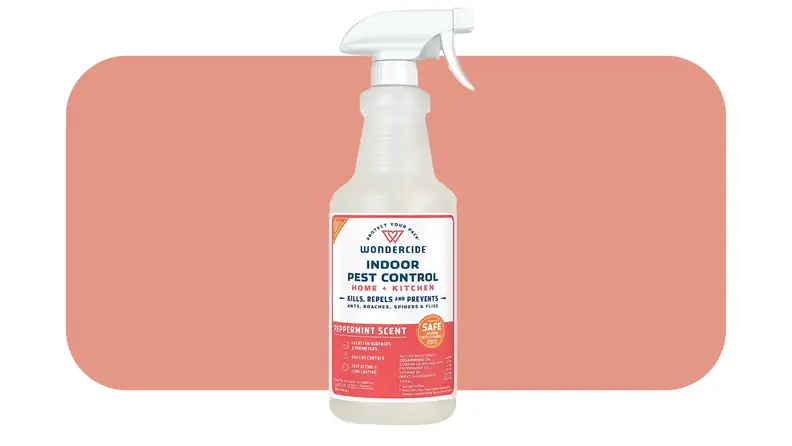 Plastic spray bottle with red label of the Wondercide Indoor Pest Control Spray  in front of pink background..