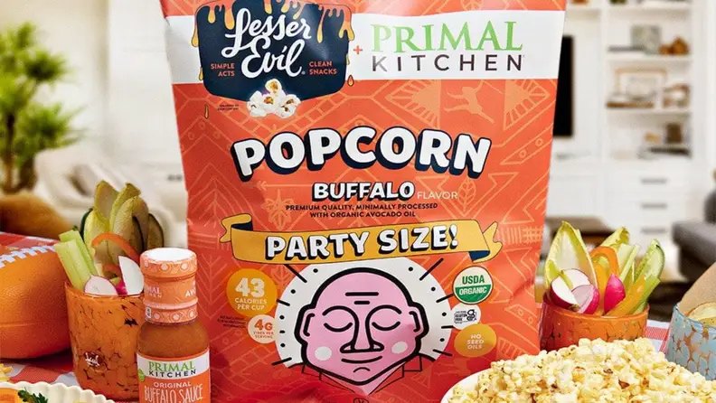 LesserEvil buffalo popcorn bag beside Primal Kitchen buffalo sauce and veggies