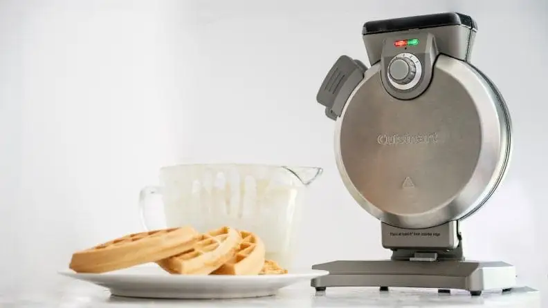 A Cuisinart waffle maker perched on a countertop next to a stack of freshly made waffles.