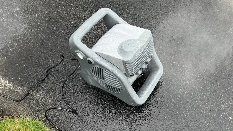 The Lasko Misto fan dripping with water and surrounded by wet pavement.