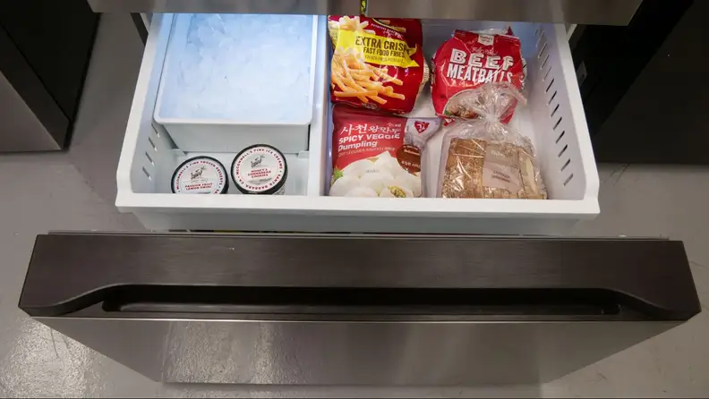 A close-up of the open freezer drawer, with the inset drawer pulled out. You can see the ice reservoir on the left and the remaining space is holding various frozen foods.