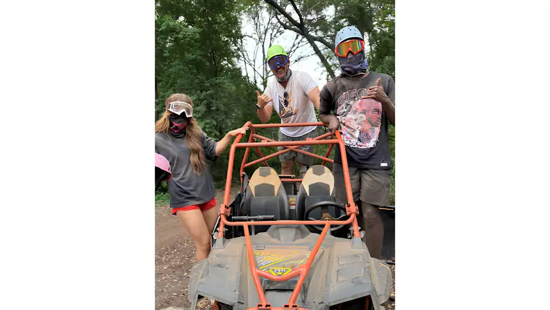 Group posing beside an off-road ATV after a muddy outdoor adventure.