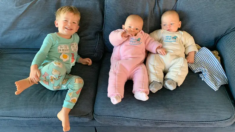A toddler and two infants sit on a blue couch.