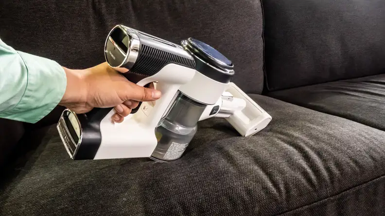 A close up of a person using the Tineco Pure One vacuum to clean a grey sofa.
