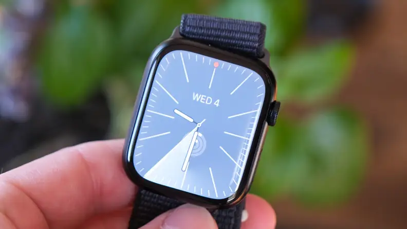Person holding the Apple Watch Series 9 in their fingers outdoors.