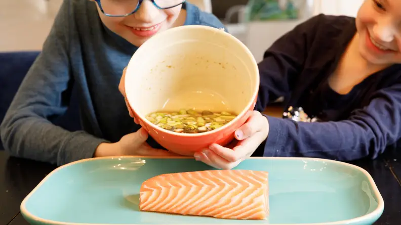 A boy and a girl pouring marinade on a piece of salmon