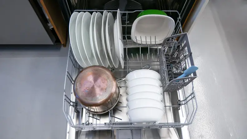 A close-up of the dishwasher's bottom rack, stocked with dishes. You can see a column of foldable tines folded down to make room for a large pot.