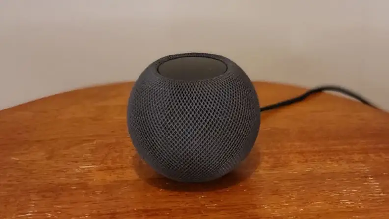 Apple's HomePod Mini smart speaker sits on a wood table.