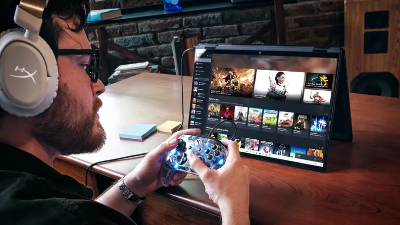 Person using a game controller with an HP gaming laptop displaying the Xbox Game Pass library.