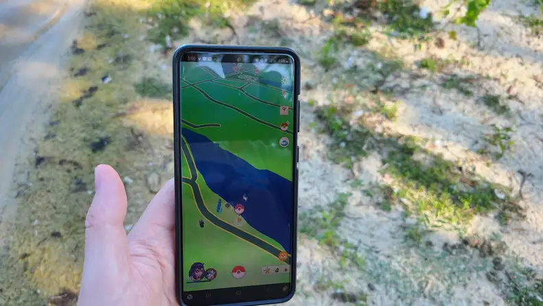 A person holding a smartphone outside, featuring the Pokémon Go Plus + app on the screen.