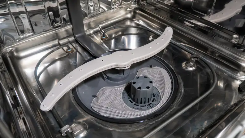 A shot of the bottom of the GE GDP645SYN0FS dishwasher's interior. We can see its spray arm and a large, clearly labeled filter.