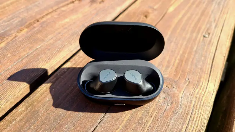 The black and silver Elite 7 Pro earbud sit in their case on a cedar bench.