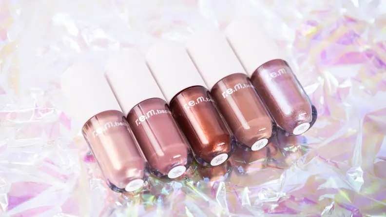 Five liquid eyeshadows in warm tones laying on holographic cellophane.
