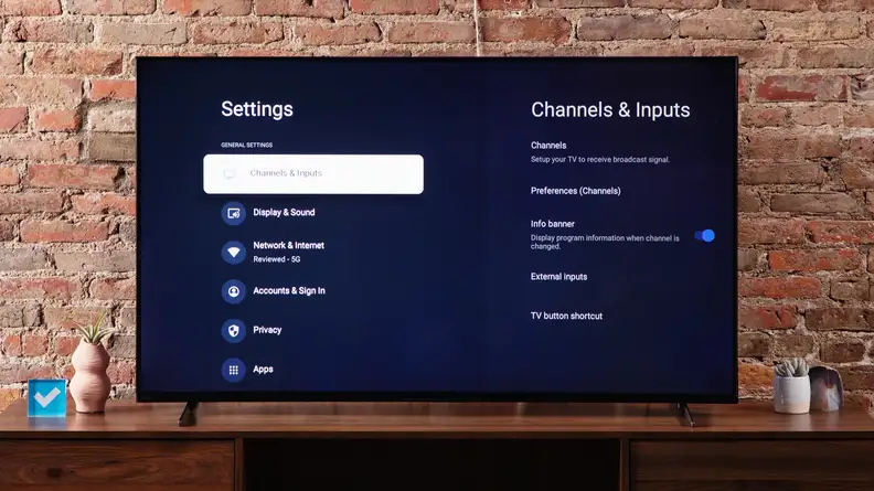 The Sony X90K LED TV on a media console in front of a brick wall, displaying its settings menu on the screen