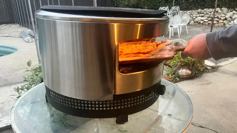 Person using a wooden pizza peel to slide into the Solo Stove Pi Prime