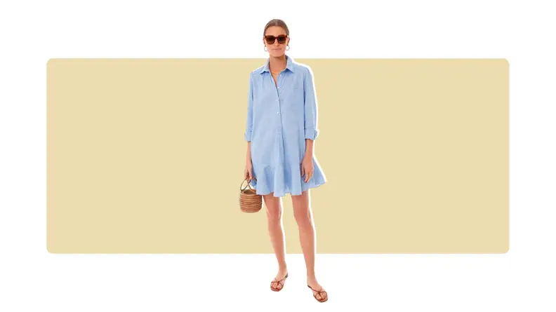A chambray shirt dress that has a ruffled hem, a half-button, and long sleeves.