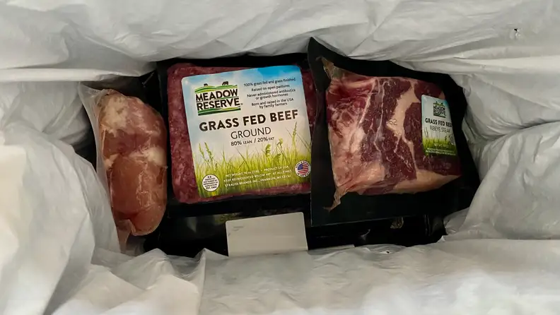 Looking into a chilled bag, there's a package of ground beef, a steak, and a package of chicken thighs.