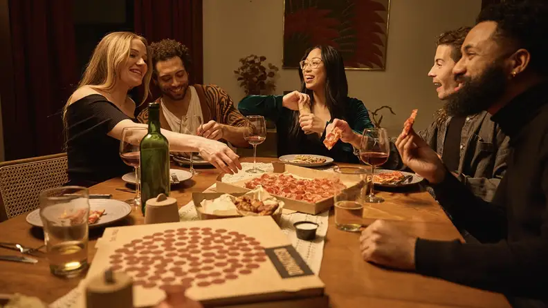 Friends sharing pizza and wings around a dinner table